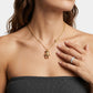 A close-up of a model wearing a delicate gold chain necklace with a small teddy bear pendant and a small gold bead accent. The model is wearing a dark gray strapless top and has a silver ring on her finger, set against a clean white background.