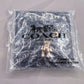 A Coach New York branded clear plastic poly bag containing a gold-tone horse logo charm, photographed on a light fabric background.
