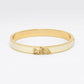 A gold-plated bangle bracelet with a cream-colored inlay and a small horse-drawn carriage charm, shown on a plain white background.