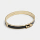 A gold-tone Coach bangle bracelet with a black enamel inlay and a small horse-and-carriage charm, shown on a light gray background.