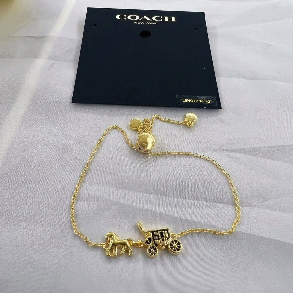 A gold-tone Coach New York bracelet featuring a horse-drawn carriage charm, displayed on its black branded hang card over a light gray fabric background.