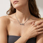 A close-up lifestyle shot of a model wearing a delicate silver necklace with a horse-drawn carriage pendant. The necklace is shown on a model's neck, with her hand resting on her chest, wearing a matching silver ring.