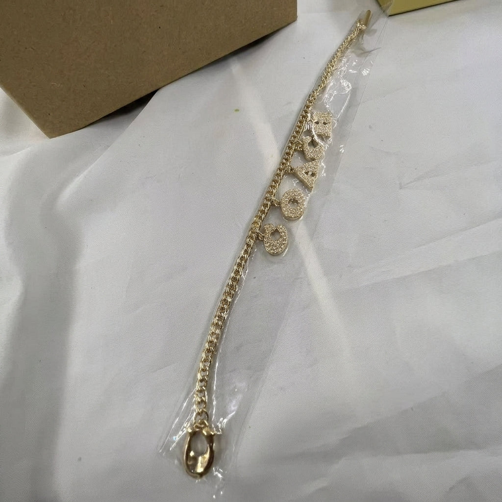 A gold chain bracelet with multiple oval and round charms, shown inside a clear plastic protective sleeve on a white surface.