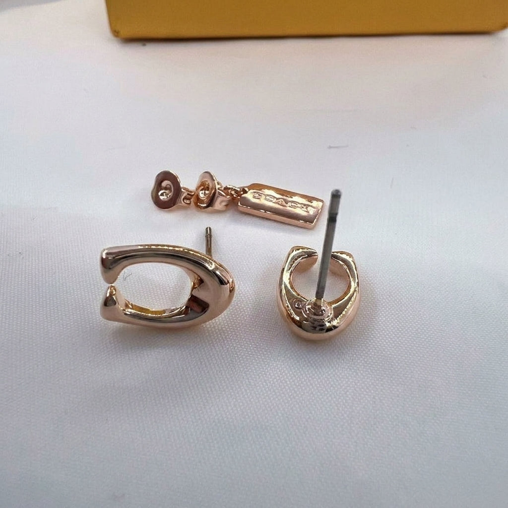 Rose gold hoop earrings shown from multiple angles on a white textured surface, with a yellow box partially visible in the background.
