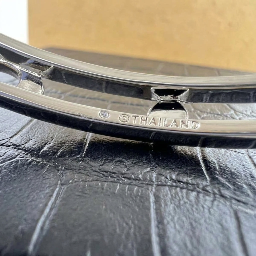 Close-up of a polished silver-toned metal bracelet or bangle resting on a black textured surface, with the word THAILAND engraved on the inside.