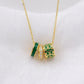 A gold chain necklace with three cylindrical charms in green and gold, displayed on a textured white fabric background.