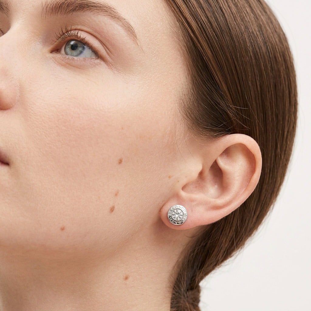 A close-up of a woman's ear wearing a round silver stud earring with a textured, diamond-like silver pattern, set against a clean white background.