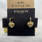 A pair of Coach heart-shaped drop earrings with gold-tone hoops and colorful enamel detailing, displayed on a black Coach New York card against a brown Coach box.