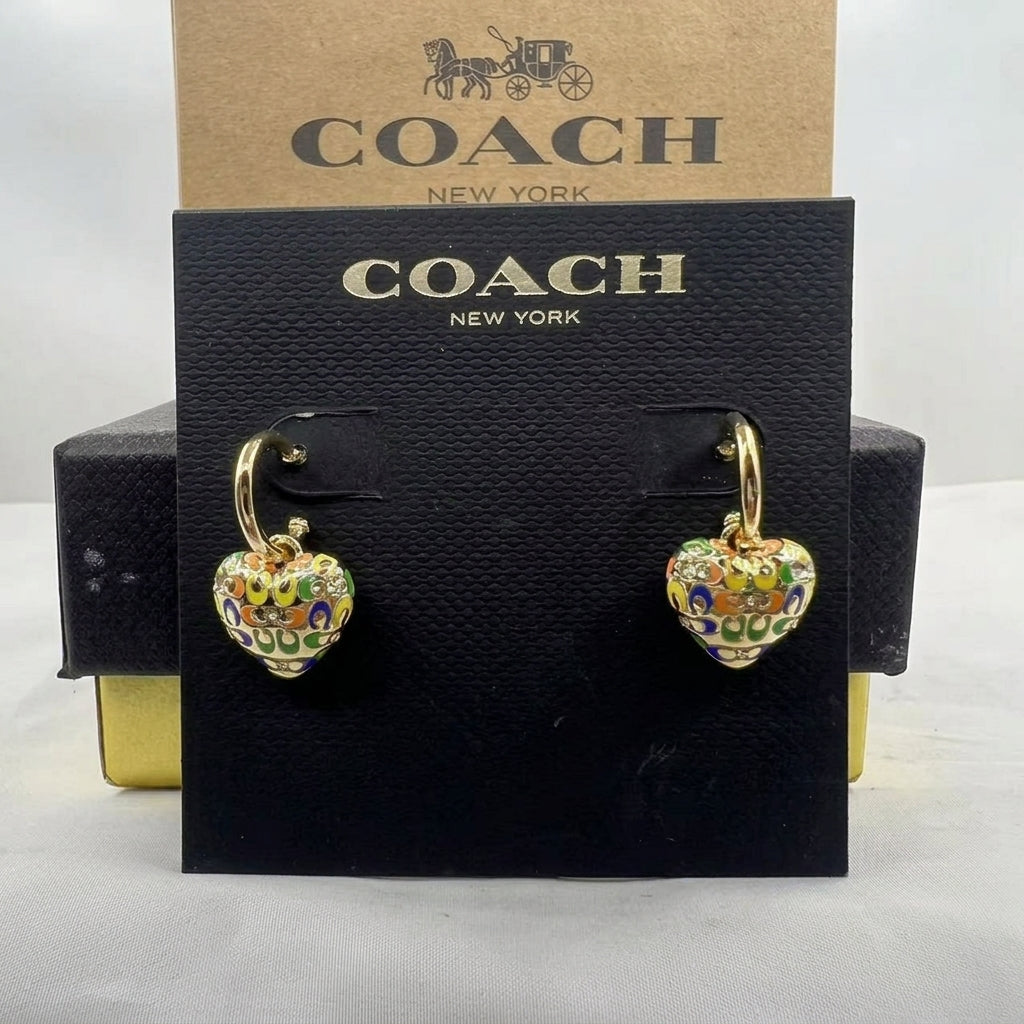 A pair of Coach heart-shaped drop earrings with gold-tone hoops and colorful enamel detailing, displayed on a black Coach New York card against a brown Coach box.