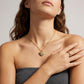 A close-up lifestyle shot of a model wearing a gold heart pendant necklace with colorful enamel details and a matching gold ring on her finger.