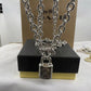 A silver-tone padlock necklace with interlocking 'CO' initials on the lock, draped over a black and gold Coach gift box with a Coach box in the background.