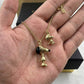 A gold-tone necklace with two character pendants, one with a black nose and one with a black ear, displayed on an open hand with a black jewelry box in the background.