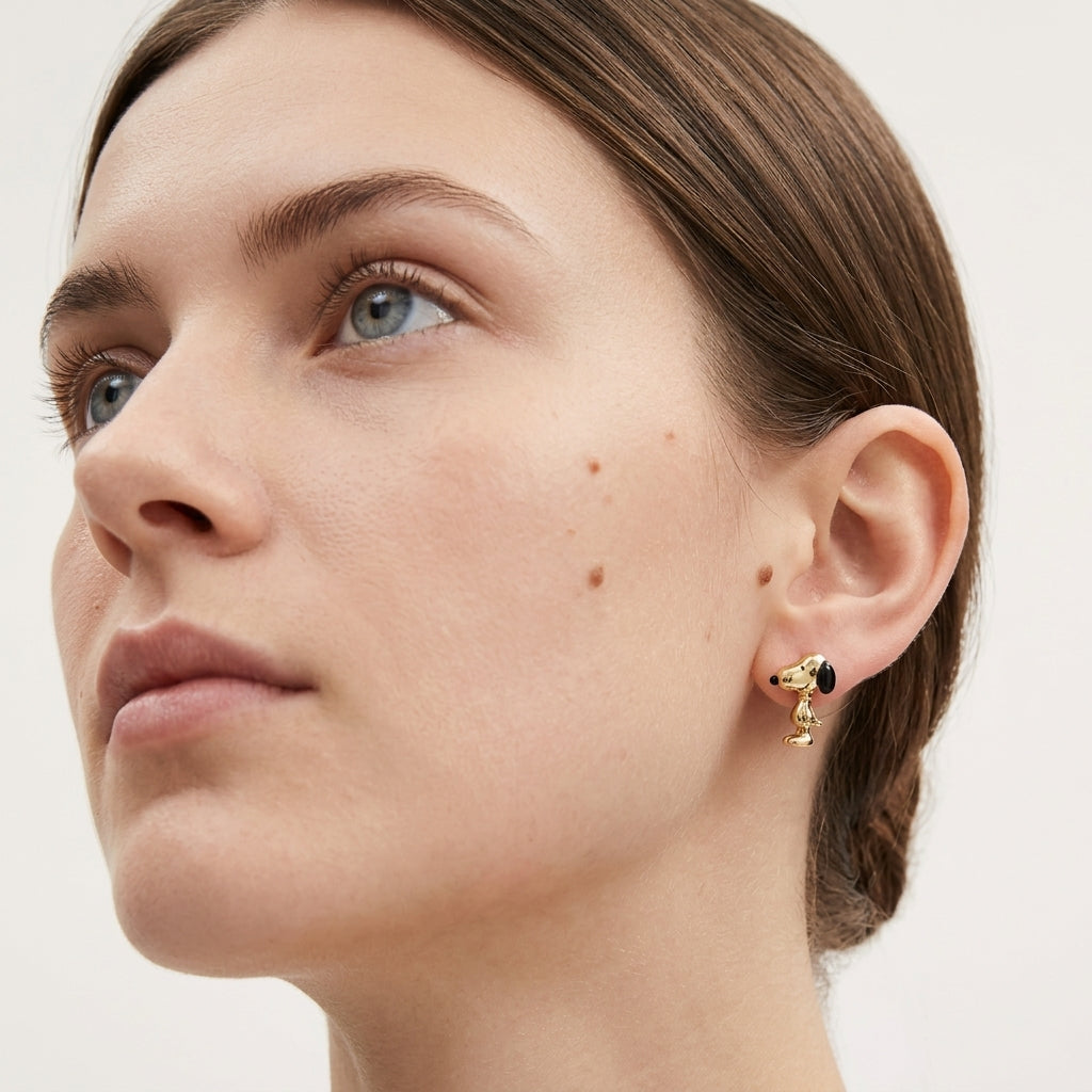 Close-up of a woman wearing a small gold hoop earring with a black and green stone cluster at the top and a dangling gold charm, shown against a plain light background.