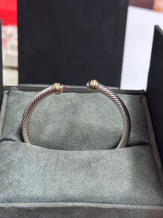 Silver bracelet with gold accents on a gray cushioned surface