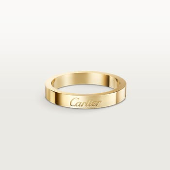 A slim yellow gold band ring engraved with the 'Cartier' logo, shown on a light gray gradient background.