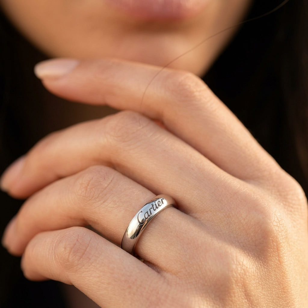 A close-up of a person's hand wearing a polished silver ring engraved with the name 'Cartier' in cursive script.