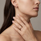 A close-up lifestyle shot of a model wearing a slim, polished rose gold band ring on her finger, with her hand resting on her neck. She also wears a matching rose gold bar stud earring.