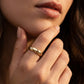 A close-up of a woman's hand and lower face wearing a slim gold band ring with engraved script lettering.