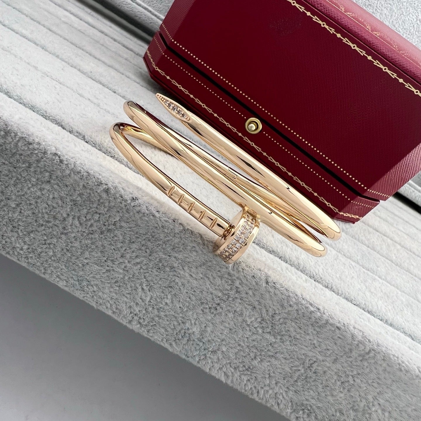 Gold bracelet and ring on a textured surface with a red jewelry box in the background