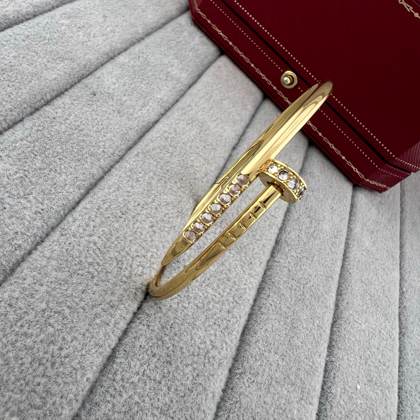 Gold bracelet with crystals on a gray surface with a red handbag in the background