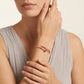 Woman wearing a rose gold bracelet with gemstones on a neutral background