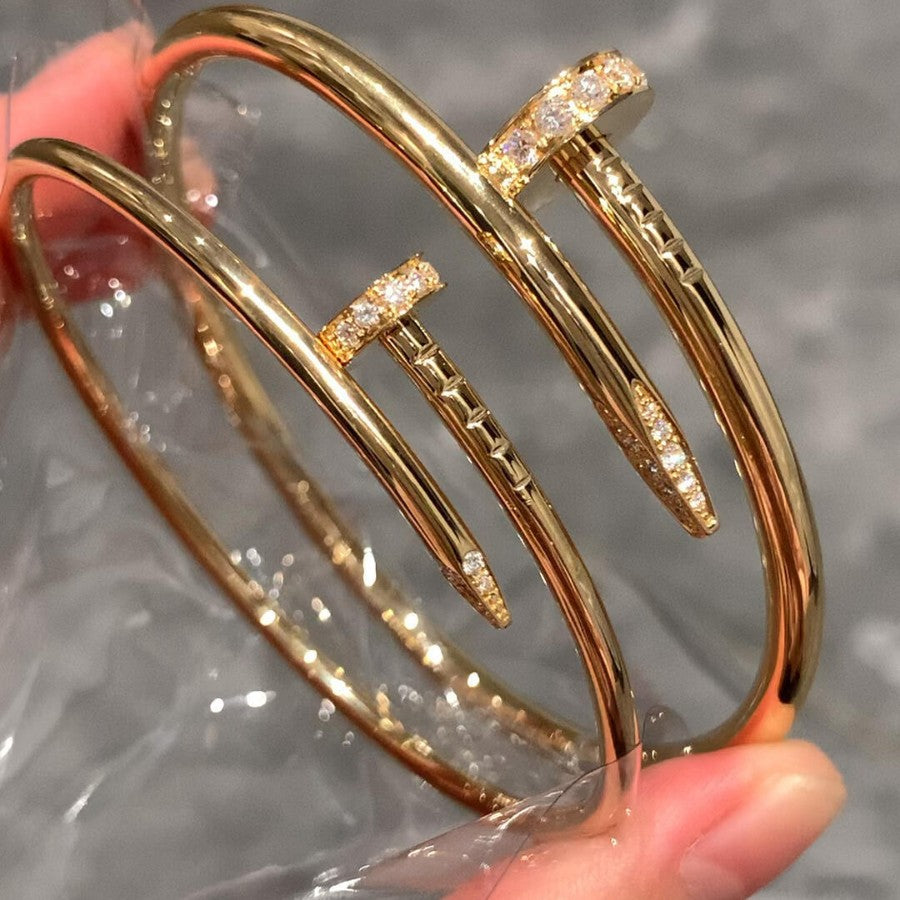 Gold bangles with diamond accents held by a hand against a gray background