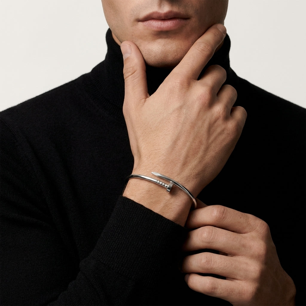 Man wearing a black turtleneck and silver bracelet, touching his chin.