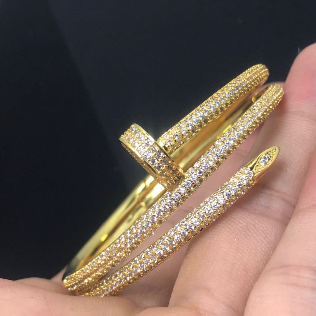 Gold bangles with diamond-like stones on a hand against a black background