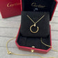 A gold Cartier necklace with a circular pendant displayed inside an open red Cartier jewelry box on a gray textured surface.