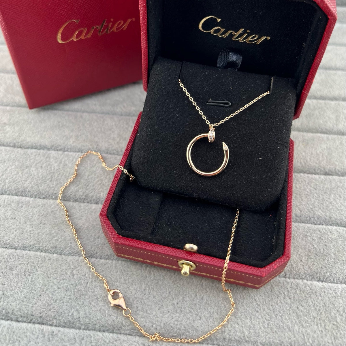 A gold Cartier pendant necklace with a circular ring and a small pavé-set stone, displayed inside an open red Cartier jewelry box on a gray textured surface.