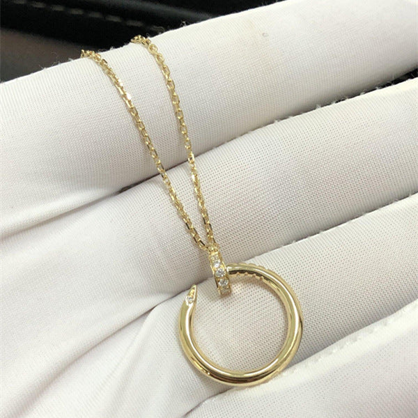 A gold necklace with a circular open pendant and a small clear stone accent, displayed on a white textured fabric surface.