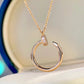 A gold-toned necklace with a circular open hoop pendant, featuring a small clear gemstone accent on the top curve, displayed against a soft cream background.