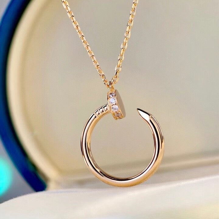 A gold-toned necklace with a circular open hoop pendant, featuring a small clear gemstone accent on the top curve, displayed against a soft cream background.