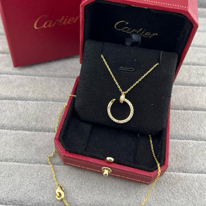 A gold pendant necklace with a small clear stone-set crescent or hoop pendant, displayed inside an open red Cartier jewelry box on a black velvet insert. The Cartier branding is visible on the inside lid and on the red box.