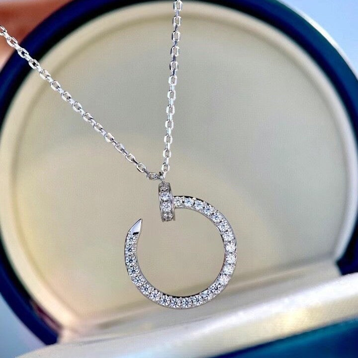 A silver necklace with a circular open pendant paved with small clear stones, displayed inside an open round jewelry box.