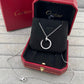 A silver crescent moon pendant necklace with a pavé-set top, displayed inside an open red Cartier jewelry box on a gray textured surface, with the Cartier box lid in the background.