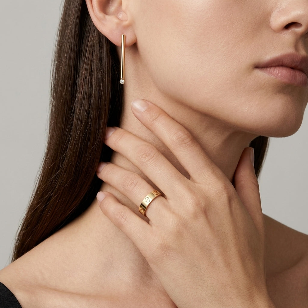 Close-up of a woman wearing gold earrings and a ring on a neutral background