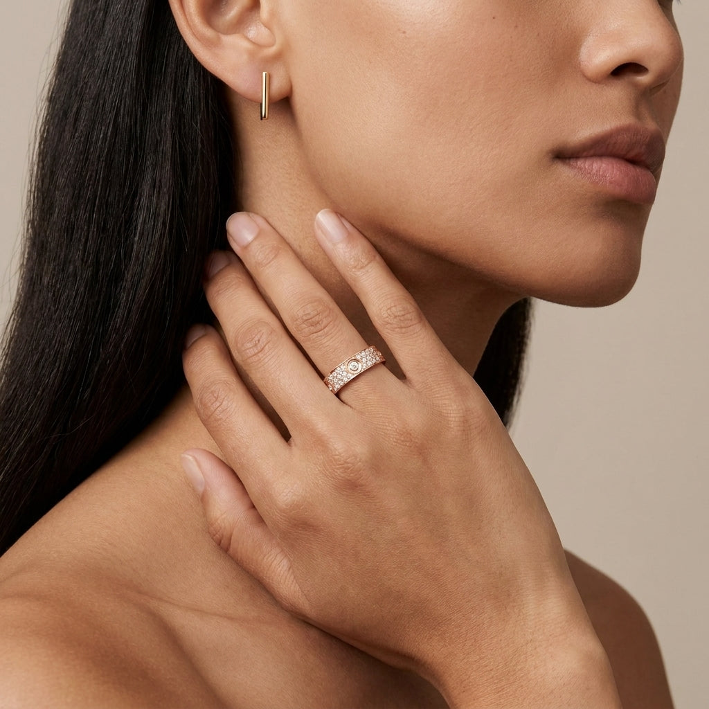 Close-up of a woman wearing a gold earring and diamond ring on a neutral background