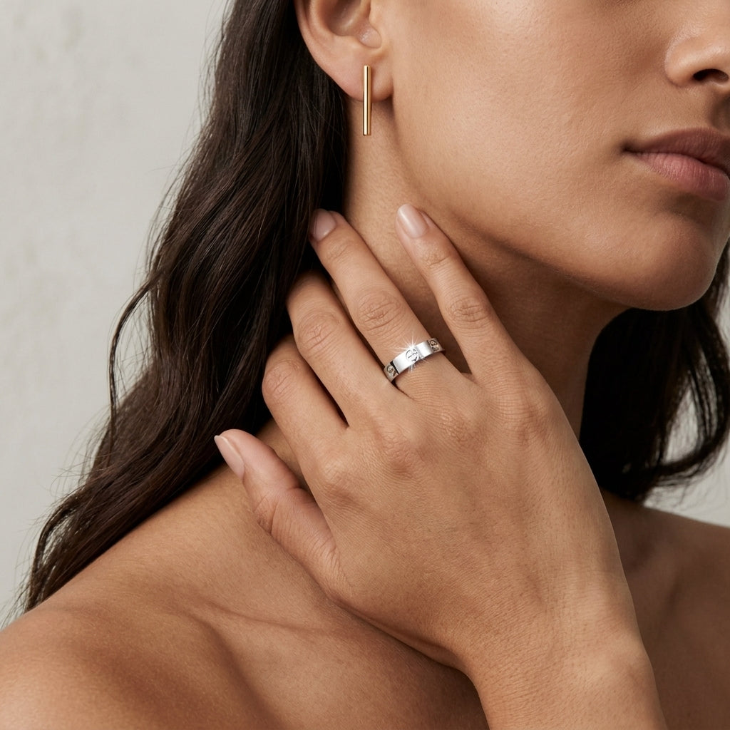 Close-up of a woman wearing a gold earring and silver ring on a neutral background