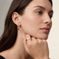 Woman wearing gold hoop earrings and ring, looking to the side.