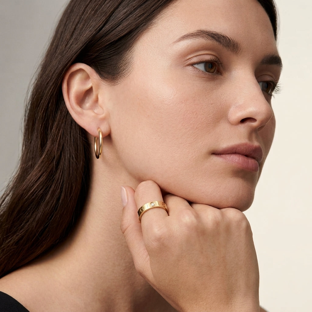 Woman wearing gold hoop earrings and ring, looking to the side.