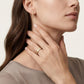 Close-up of a woman wearing gold hoop earrings and a ring on a neutral background