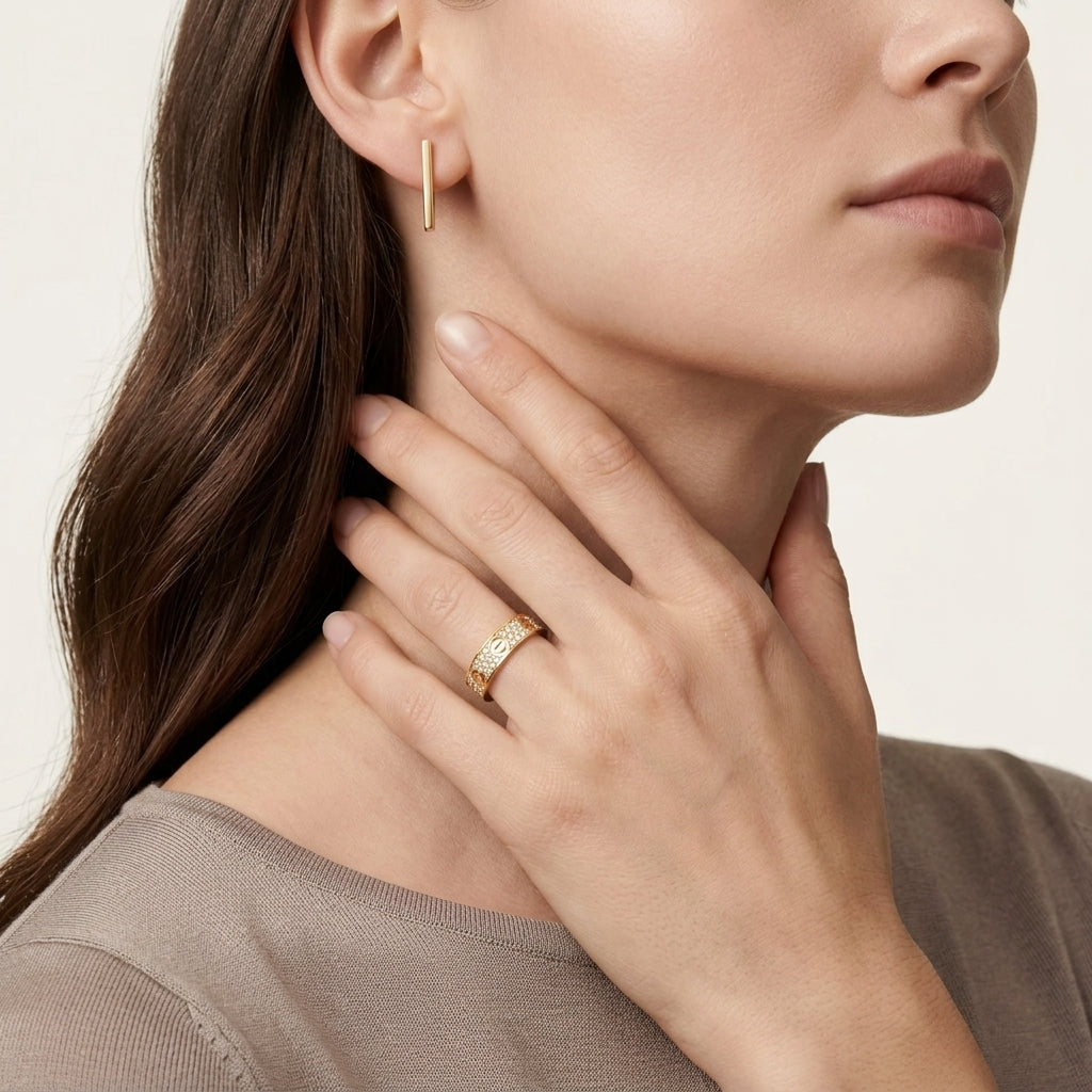 Close-up of a woman wearing gold hoop earrings and a ring on a neutral background