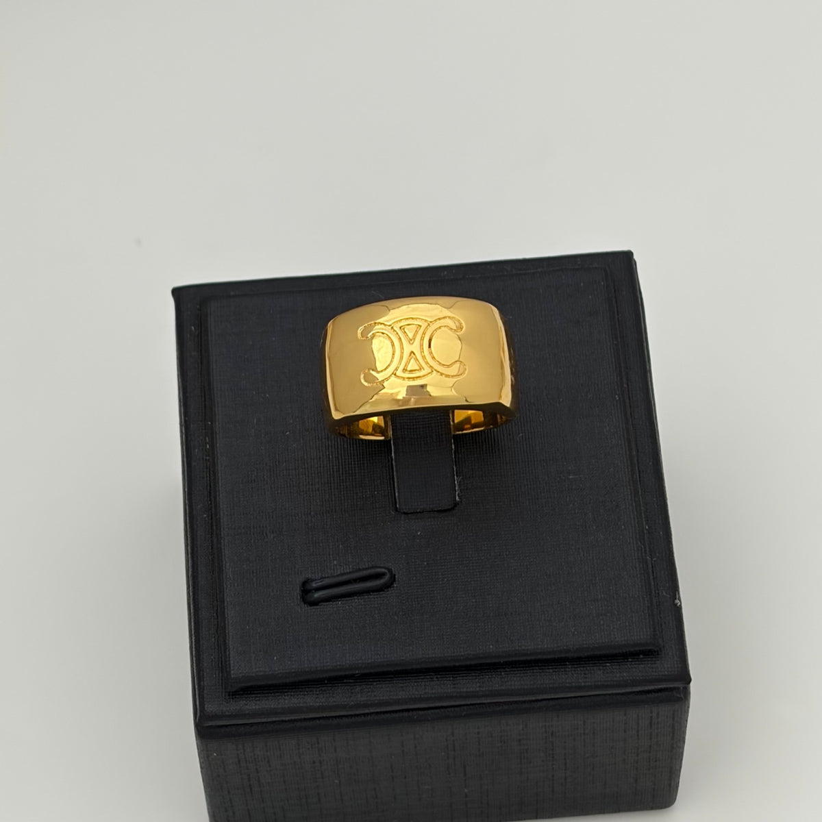 A gold signet-style ring with an engraved double-C logo, displayed on a black presentation box against a light gray background.