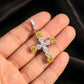 Gold cross pendant with yellow gemstones held in a hand against a dark background