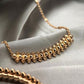 Clash de Cartier pendantGold necklace with pyramid-shaped beads on a gray fabric background