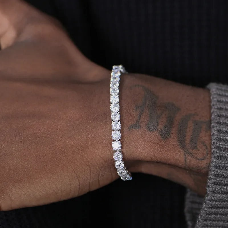 Silver bracelet on a wrist with tattoos, against a dark background