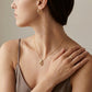 A close-up lifestyle shot of a model wearing a delicate gold chain necklace with a small teardrop pendant and a matching gold hoop earring, paired with a taupe camisole against a neutral beige background.