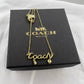 A gold-tone Coach name necklace with a 'Coach' script pendant, a small teardrop charm, and a heart charm, displayed on top of its black branded box.