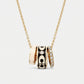 A gold chain necklace with a multi-band pendant featuring gold, black enamel, and diamond accents, shown on a light gray background.